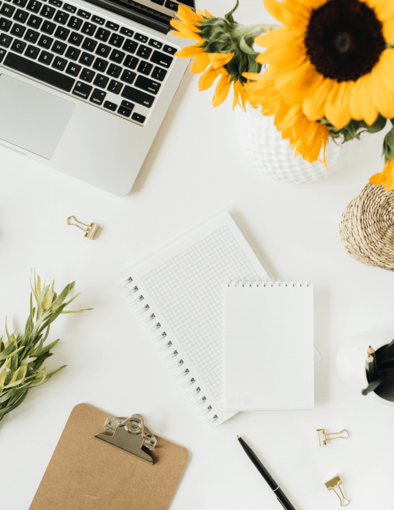 laptop, sunflowers, notebook, clipboard on white desk