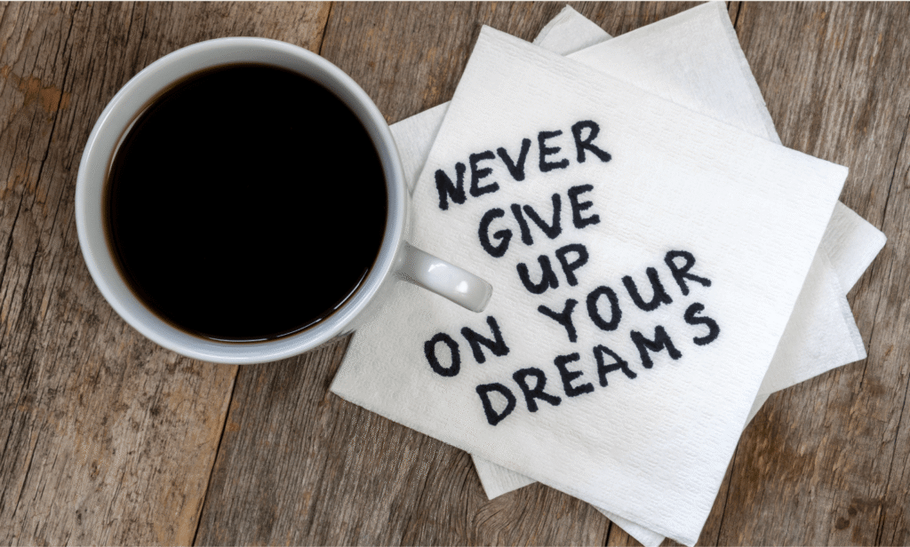 Top of coffee cup with stack of white napkins with Never Give Up on Your Dreams written out