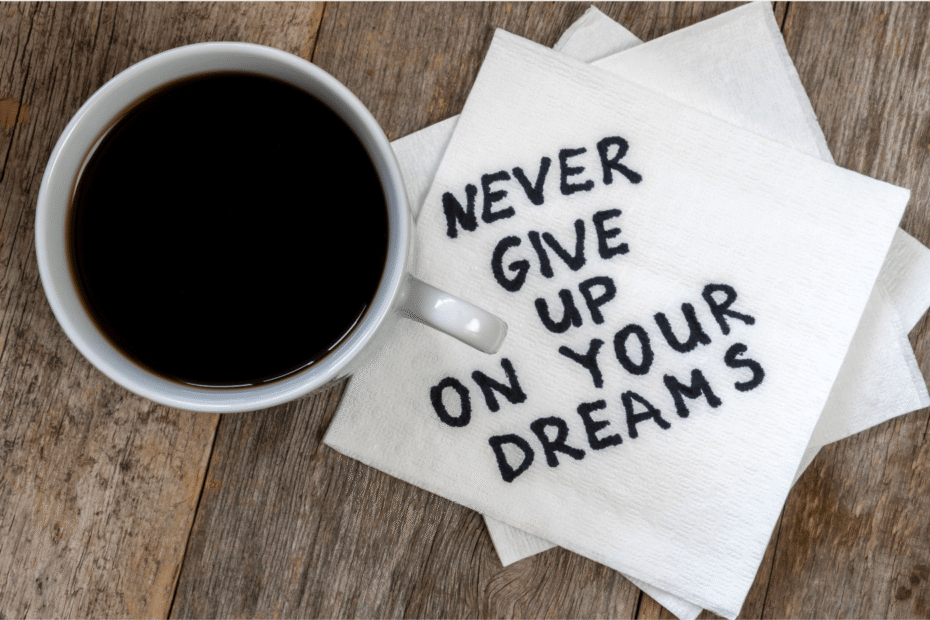 Top of coffee cup with stack of white napkins with Never Give Up on Your Dreams written out