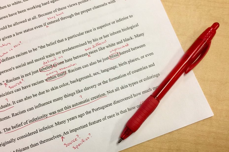 paper with red pen and edits in red on desk